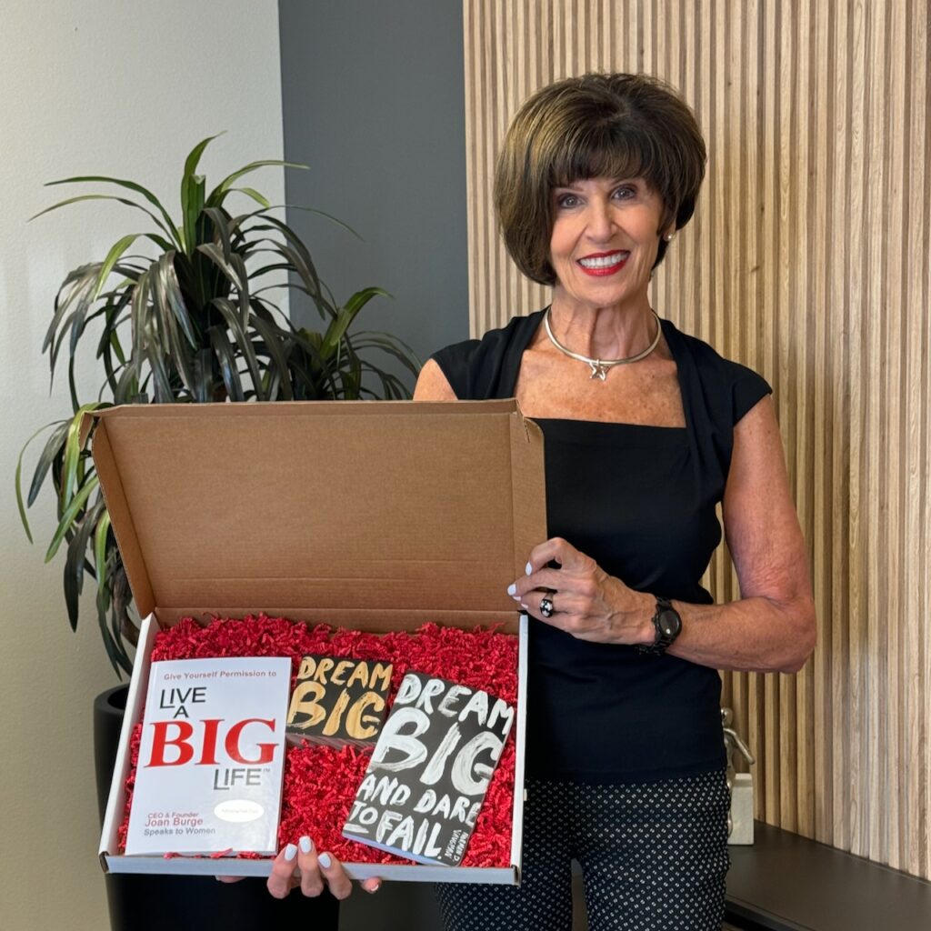 Joan Burge holding a box containing her How to Live a Big Life book, a journal, and other items