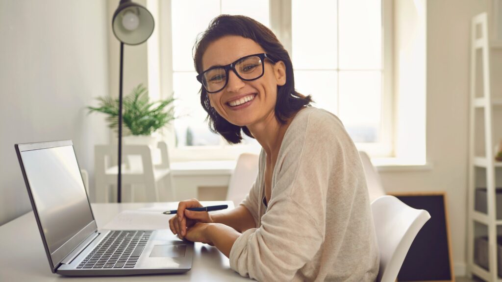 Smiling young woman in glasses sitting at a desk in front of a laptop - image for webinar recap blog on Strategic Administrative Assistants