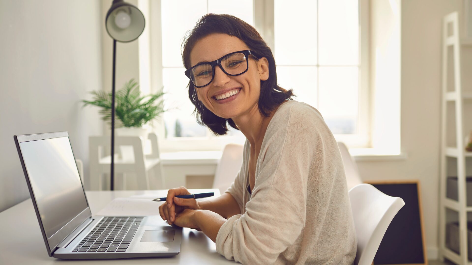 Smiling young woman in glasses sitting at a desk in front of a laptop - image for webinar recap blog on Strategic Administrative Assistants