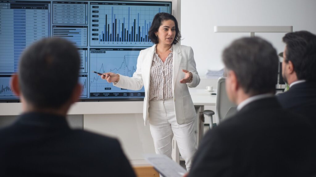 Essential Lessons for Career Growth - woman in white pantsuit presents data and graphs to three men in a conference room