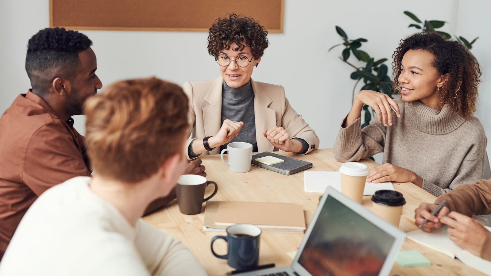 business etiquette training image is a photo of 4 professionals talking around a conference room table looking pleasant and cooperative