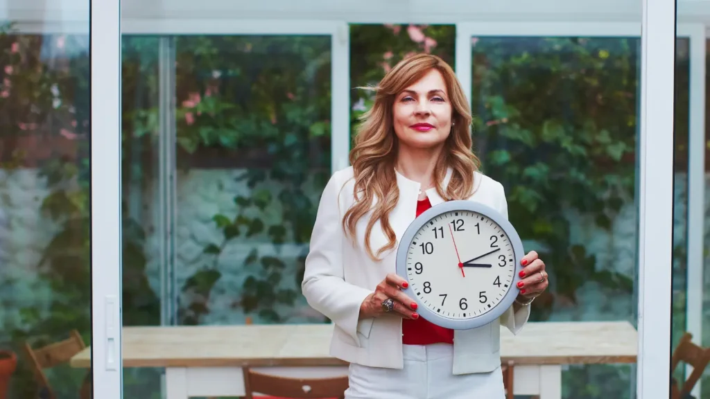 image for productivity and time management article shows woman in white pantsuit holding a clock, looking confident