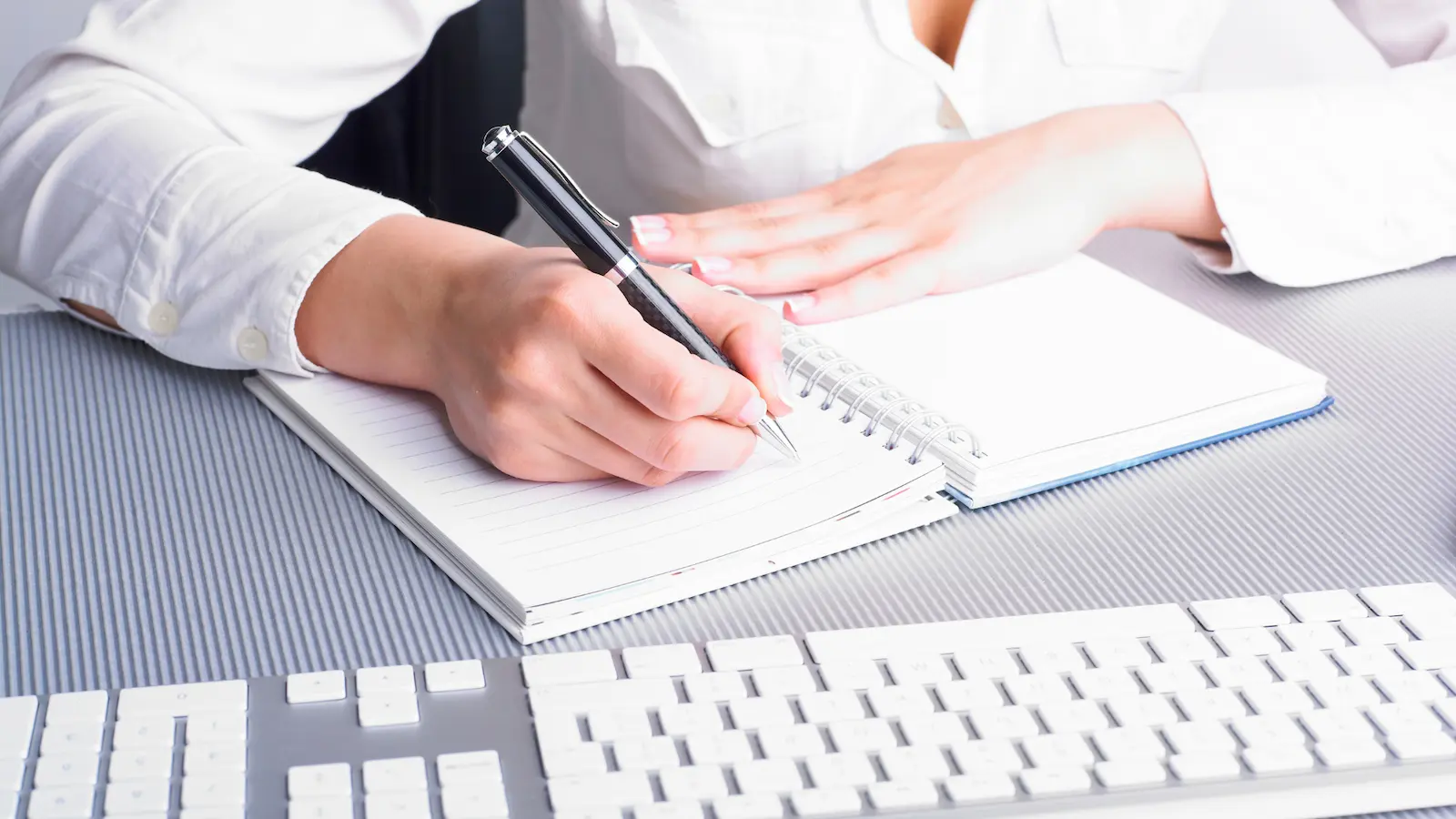 business writing skills image shows a woman writing in a journal, with her computer keyboard nearby