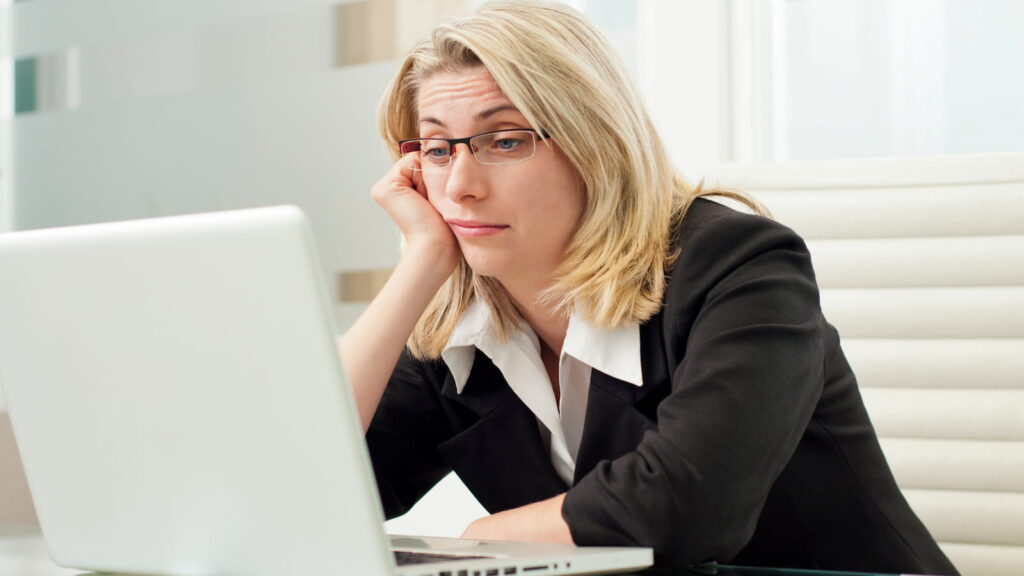 woman in business attire sitting at a computer with her chin on her hand looking bored and frustrated because she's feeling underutilized