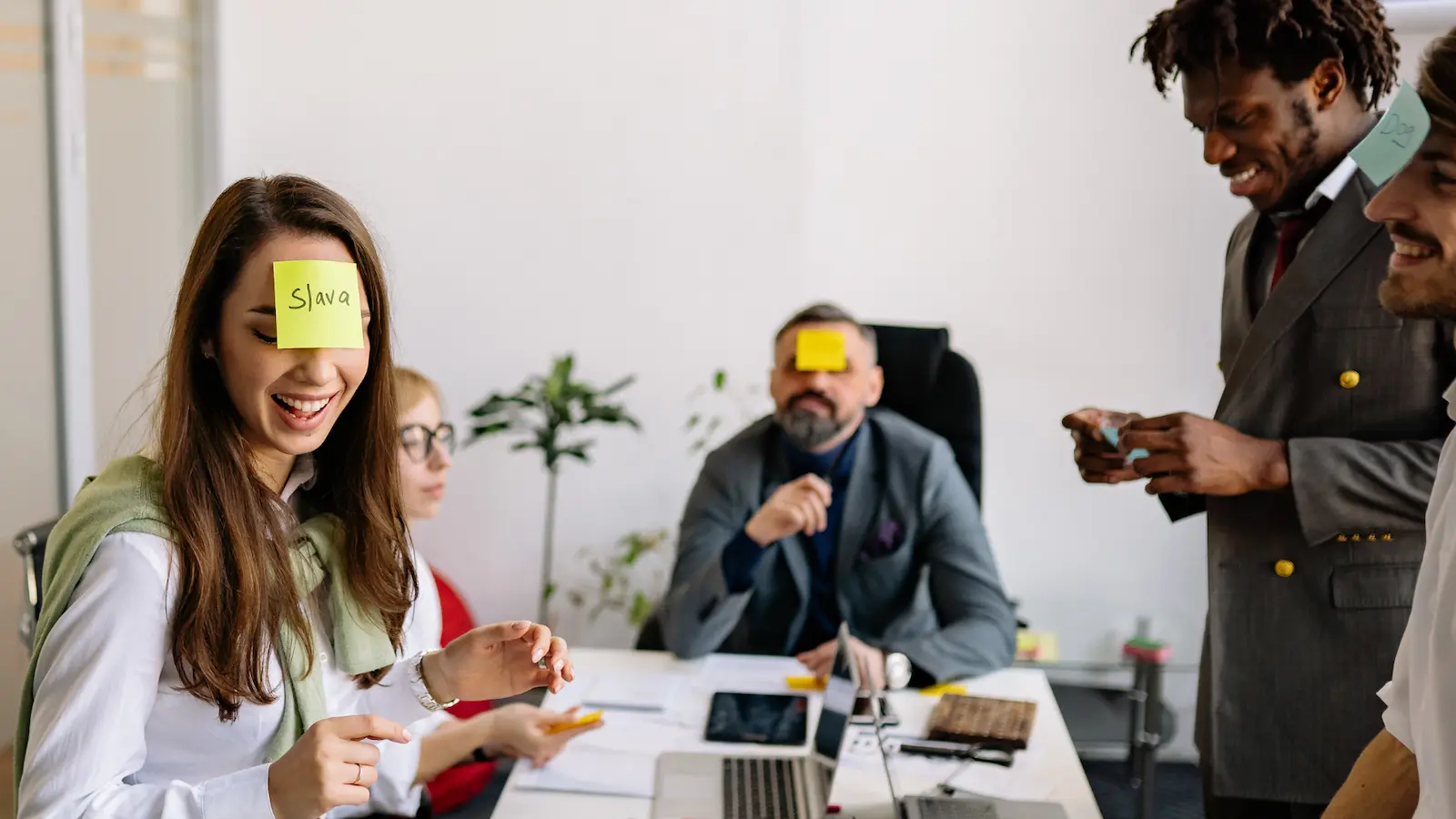 Meeting Icebreakers for Teams shows a team of professionals around a conference table with post-it notes on their foreheads. Some of them are laughing.
