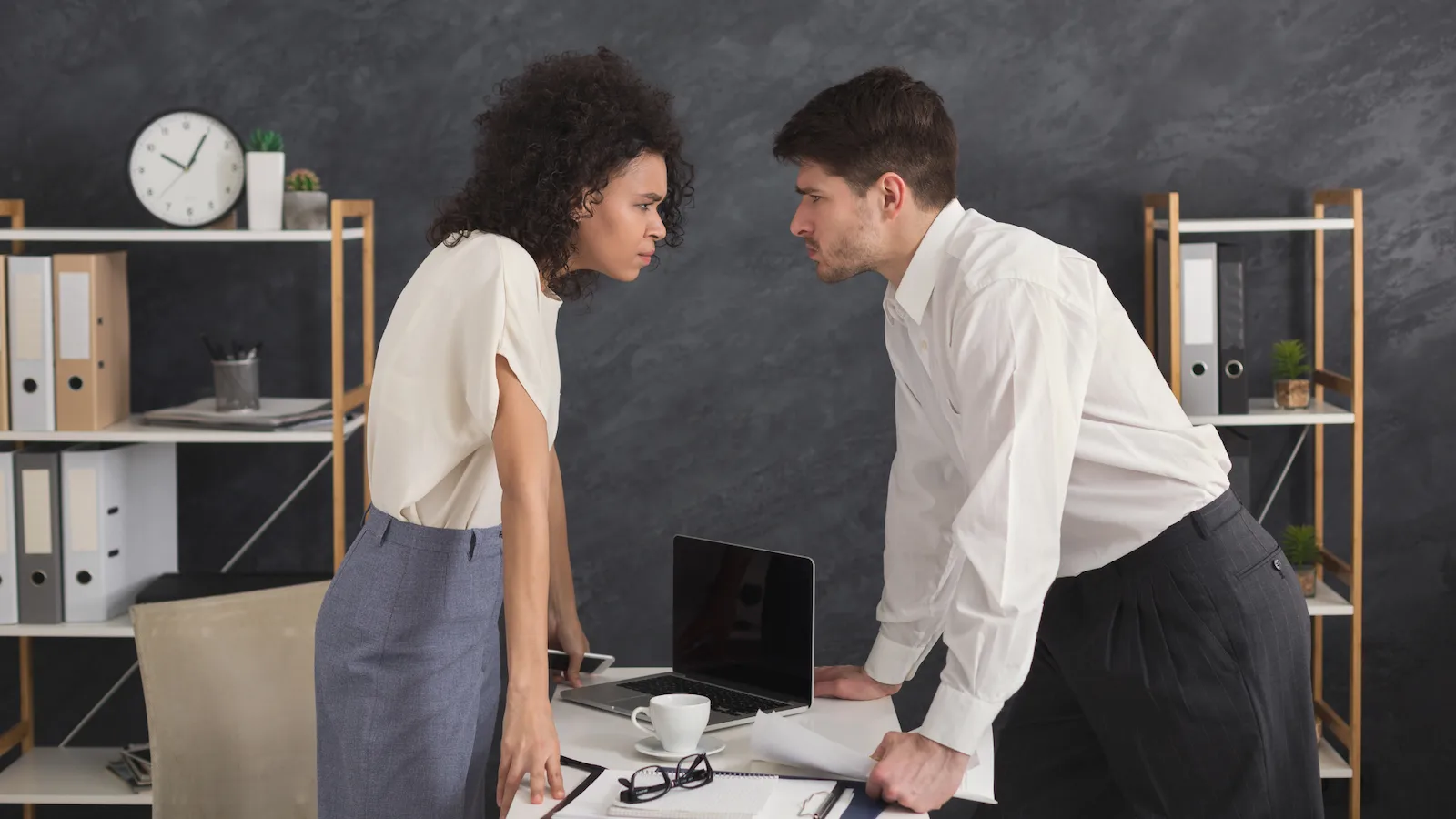 how to deal with difficult people at work blog image shows professional woman and man glaring across a desk at each other