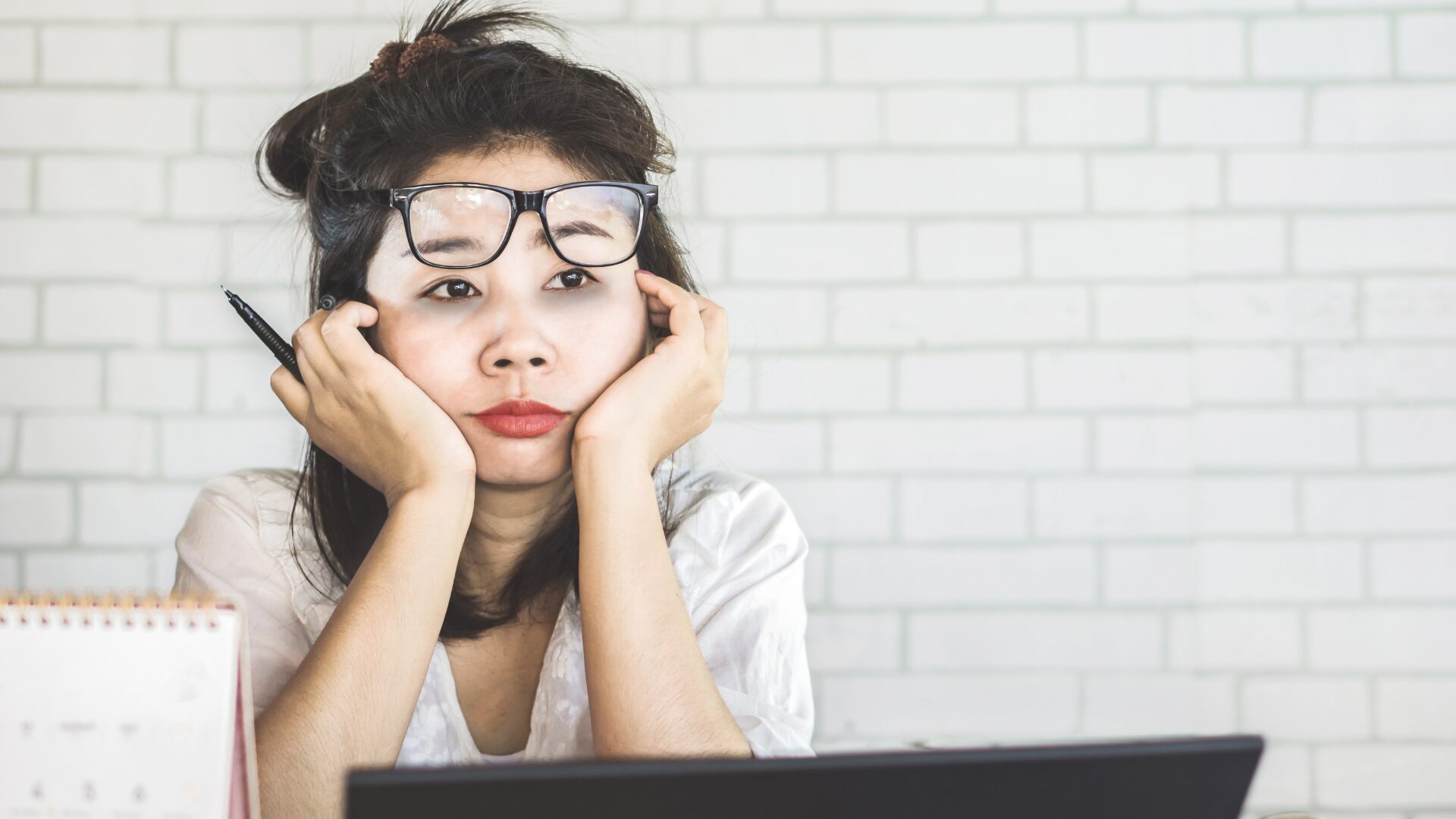 Why High-Performing Women Feel Overwhelmed and What to Do About It - Image of woman in front of a computer with her chin in her hands and glasses perched on her forehead, looking overwhelmed